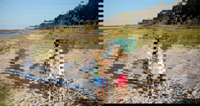 Twee kinderen staan op het strand en bekijken een brievenbus in de omgeving.