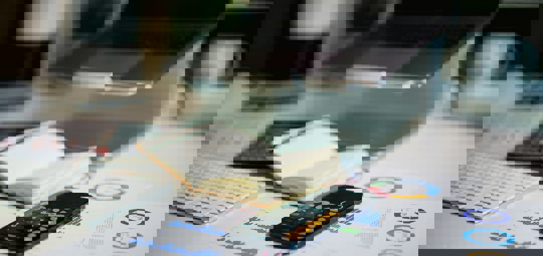 Een bureau met een laptop, een telefoon en een rekenmachine erop.