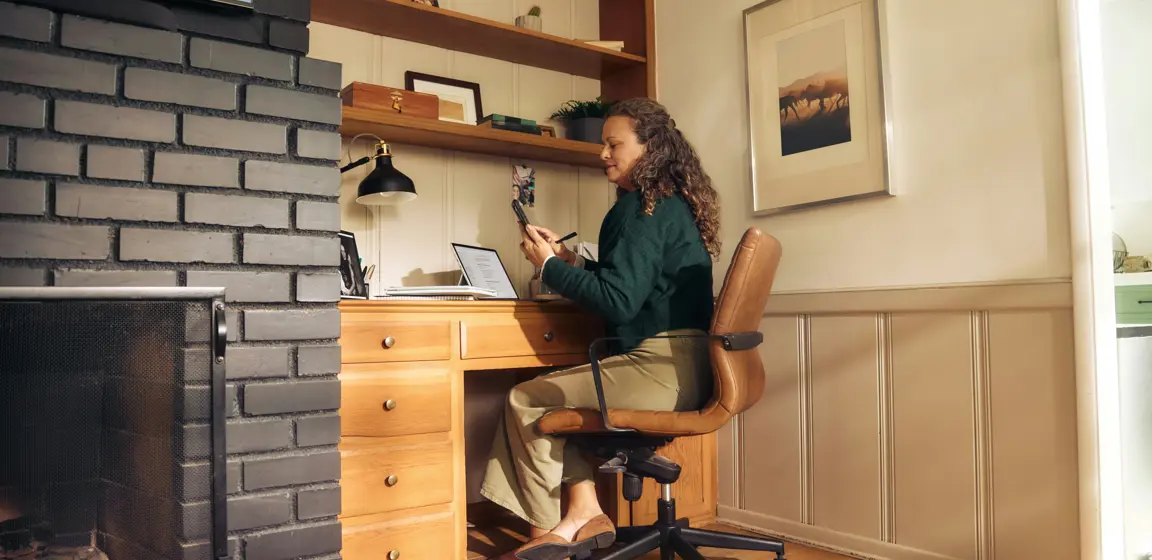Een vrouw werkt aan een bureau met een open haard op de achtergrond.