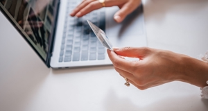 Persoon voert online betaling uit op laptop en houdt bankpas in de hand.