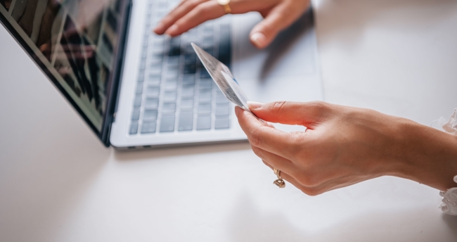 Persoon voert online betaling uit op laptop en houdt bankpas in de hand.