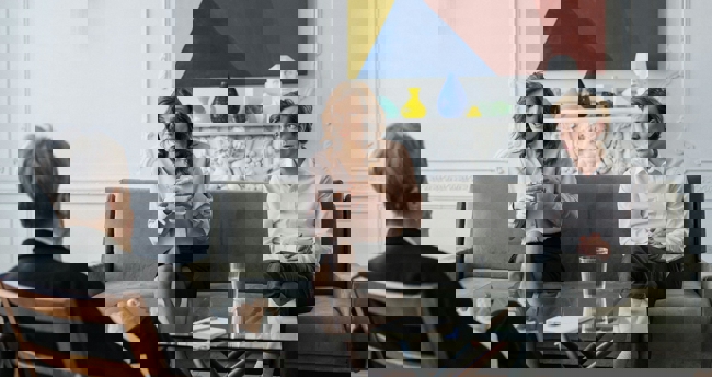 Een echtpaar en een relatietherapeut zitten in de woonkamer, in gesprek over hun scheiding.