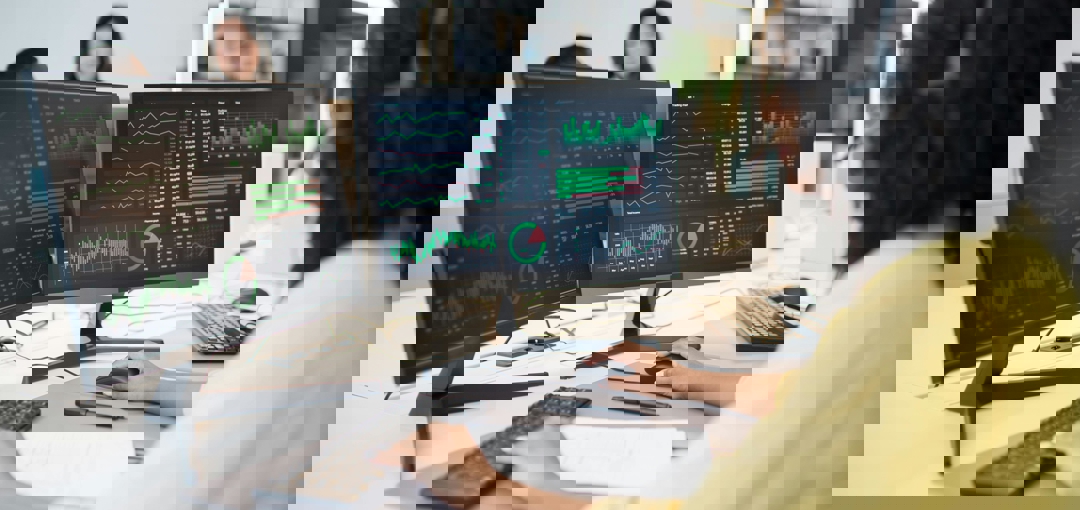 Een vrouw kijkt naar twee computerschermen terwijl ze werkt.