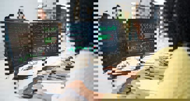 Een vrouw kijkt naar twee computerschermen terwijl ze werkt.