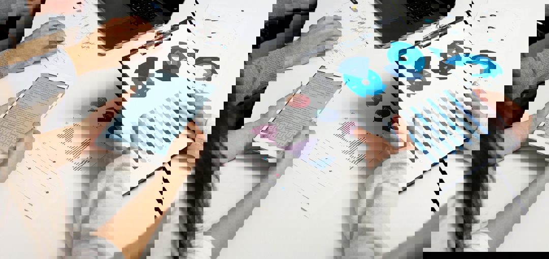 Groep mensen aan het werk met een laptop en tablet, met grafieken verspreid over de tafel.